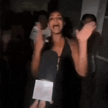 a woman in a black tank top is dancing in a dark room with a microphone .