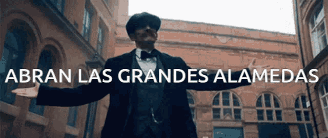 a man in a suit and tie stands in front of a building with the words abran las grandes alamedas written above him