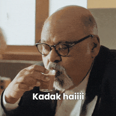 a bald man with glasses and a beard drinks from a glass with the words kadak haiiii written below him