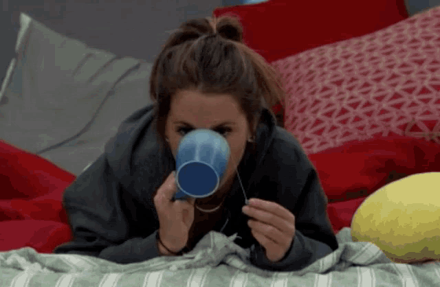 a woman is drinking from a blue cup on a bed