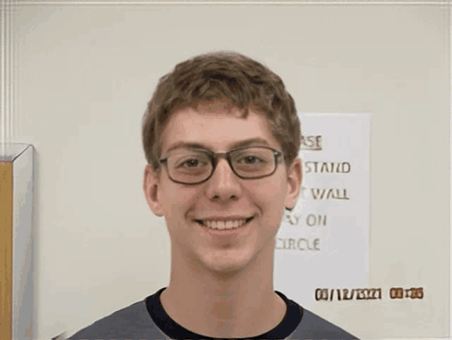 a young man wearing glasses is smiling in front of a sign that says " case stand "