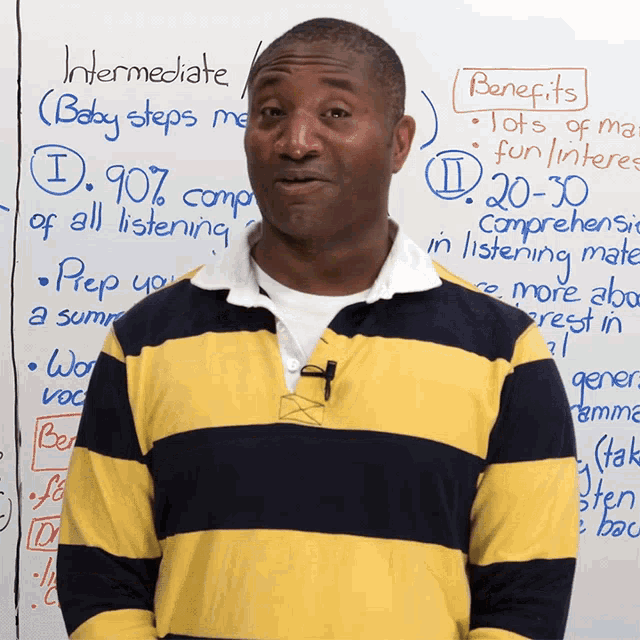 a man in a yellow and black striped shirt stands in front of a white board with intermediate written on it