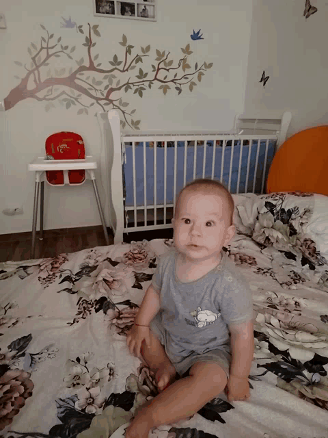 a baby is sitting on a bed with a floral blanket