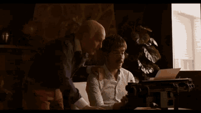 two men are sitting on a couch looking at a laptop screen .