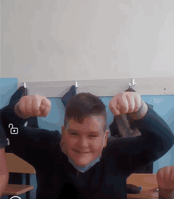 a young boy flexes his muscles in front of a wall with hooks