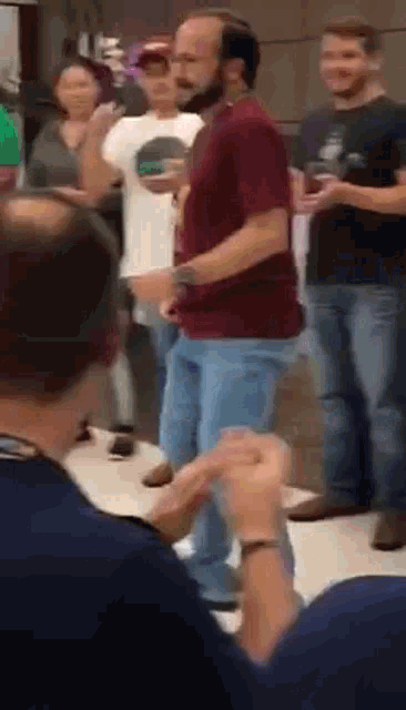 a group of people are standing around a man in a red shirt