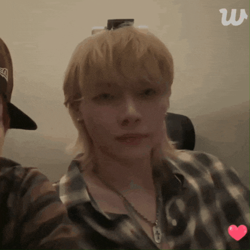 a man with blonde hair is wearing a plaid shirt and a hat with the letter w on it
