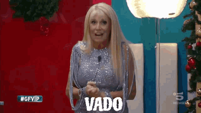 a woman in a sequined dress is standing in front of a sign that says vado