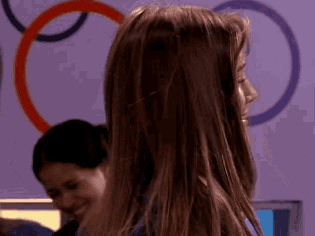 a woman with long brown hair is smiling in front of a purple wall