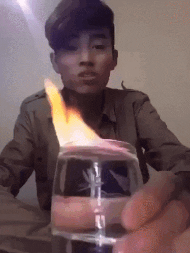 a young man is holding a glass of water with a flame coming out of it