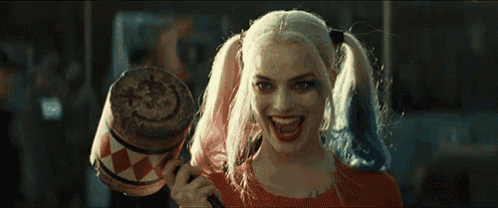 a woman in a harley quinn costume is holding a hammer and smiling .