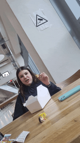 a girl sitting at a table with a box of food in front of a sign that says ' cctv '