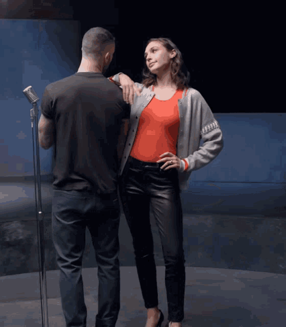 a woman in a red tank top stands next to a man in a black shirt