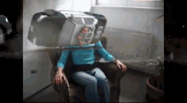 a woman in a blue shirt is sitting in a chair with a box on her head that says e50