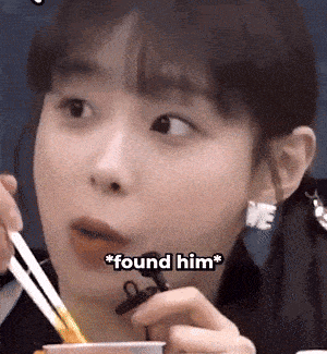 a girl is eating noodles with chopsticks and says " found him " in the corner