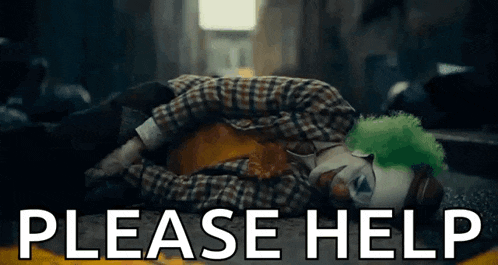 the joker is laying on the ground with the words `` please help '' behind him .