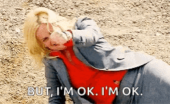 a woman in a suit and red shirt is laying on the ground and says but i 'm ok i 'm ok