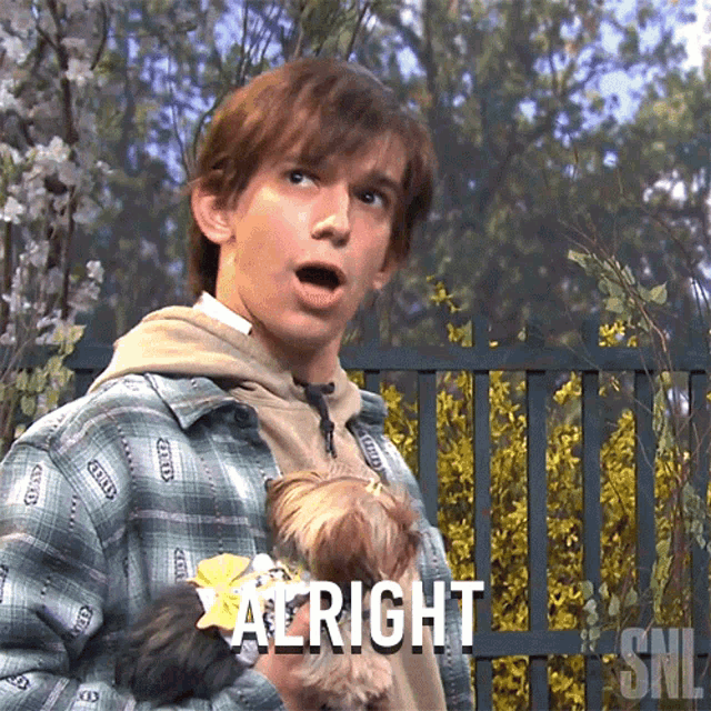 a man is holding a small dog and says " alright "