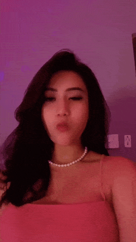 a woman in a pink top and pearl necklace is making a face .