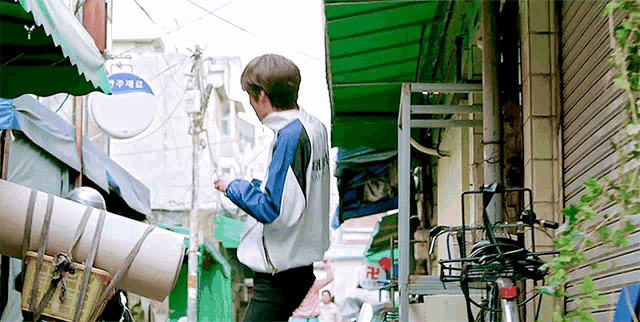 a man is walking down a narrow street with a bicycle in the foreground .