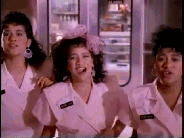 three women are standing next to each other in a room and singing .