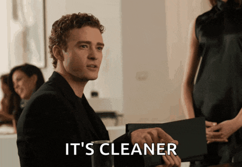 a man in a black suit is holding a black folder with the words it 's cleaner below him