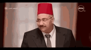 a man in a suit and tie is wearing a red hat and making a funny face .