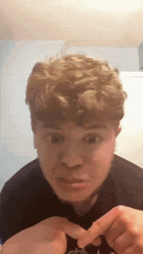 a young man with curly hair making a funny face with his fingers crossed