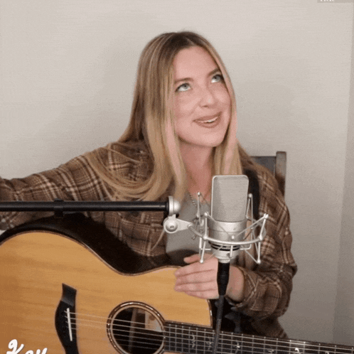 a woman singing into a microphone next to a guitar