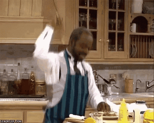 a man in an apron is standing in a kitchen with a bottle of mustard on the counter .