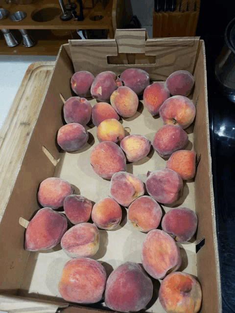 a cardboard box filled with lots of peaches on a cutting board