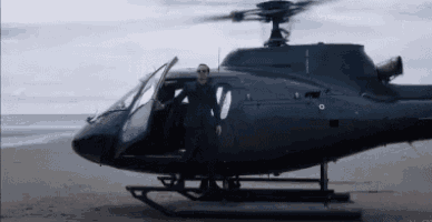 a man is standing in the doorway of a helicopter on the beach .