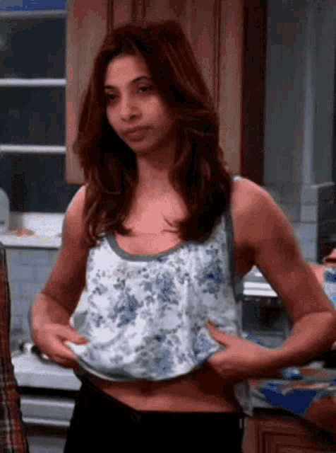 a woman in a floral tank top is taking off her top in a kitchen