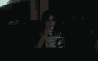 a woman is eating popcorn while watching a movie in a dark movie theater .