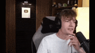 a man wearing headphones and a white shirt is sitting in front of a microphone .
