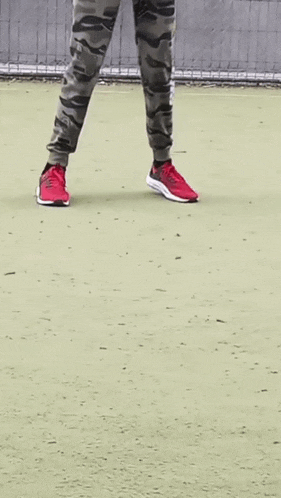 a person wearing camouflage pants and red shoes stands on a tennis court
