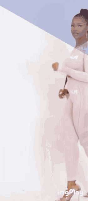 a woman is standing in front of a white wall wearing a white jumpsuit and heels .