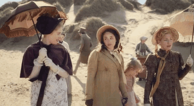 a group of women are walking on a sandy beach holding umbrellas