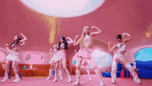 a group of young women are dancing in a room with a pink background .