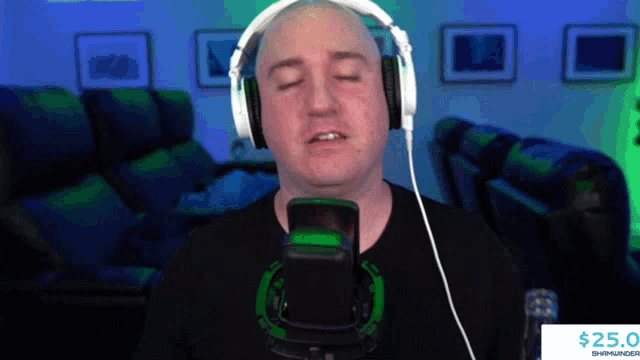 a bald man wearing headphones stands in front of a microphone and a $ 25.0 sign
