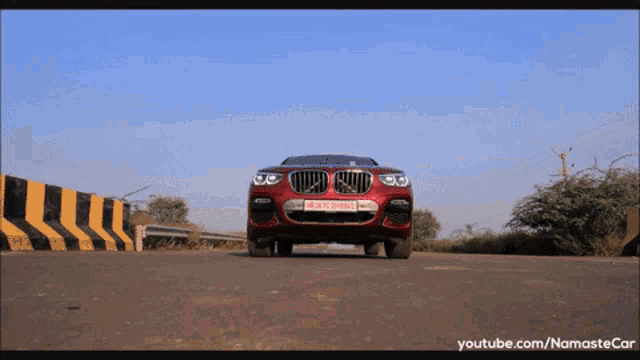 a red bmw is driving down a road with a youtube.com/namastecar watermark on the bottom