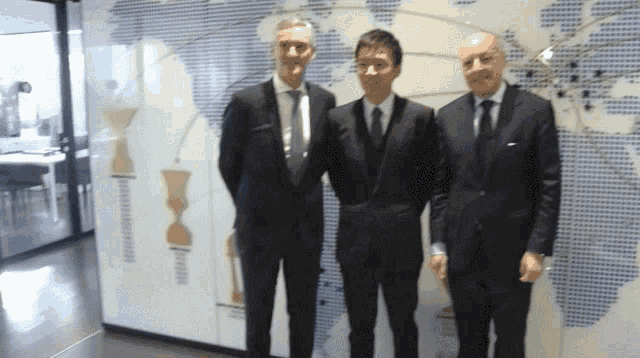 three men in suits and ties pose in front of a map of the world
