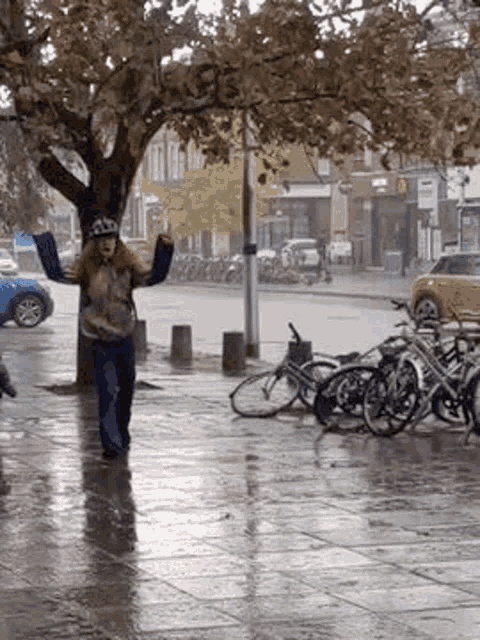 a woman is standing on a wet sidewalk in front of a row of parked bicycles .