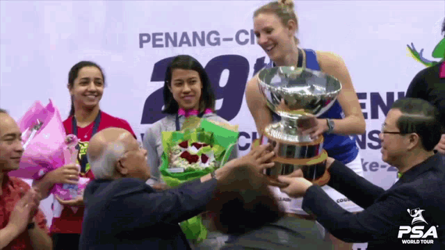 a woman holds a trophy in front of a penang-city sign