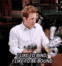 a man in a white shirt is holding a roll of tape and says i like to bind i like to be bound .
