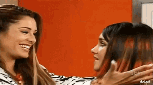 two women are hugging each other in front of an orange wall and smiling .