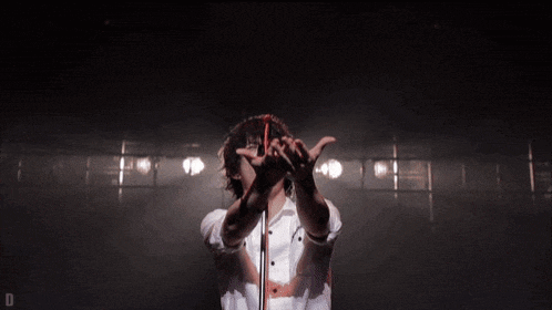 a man in a white shirt is singing into a microphone with his hands up