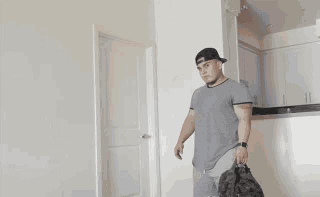a man in a gray shirt and black hat is carrying a large bag