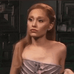 ariana grande is wearing a strapless dress and making a funny face while standing in a room .