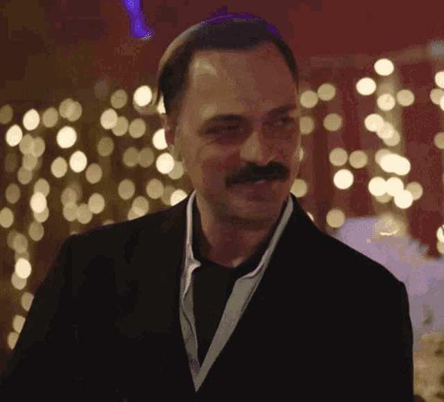a man with a mustache wearing a suit and tie is standing in front of christmas lights .